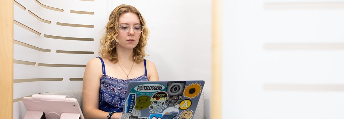 Student with curly blonde hair focuses on a laptop computer with stickers covering the outside 